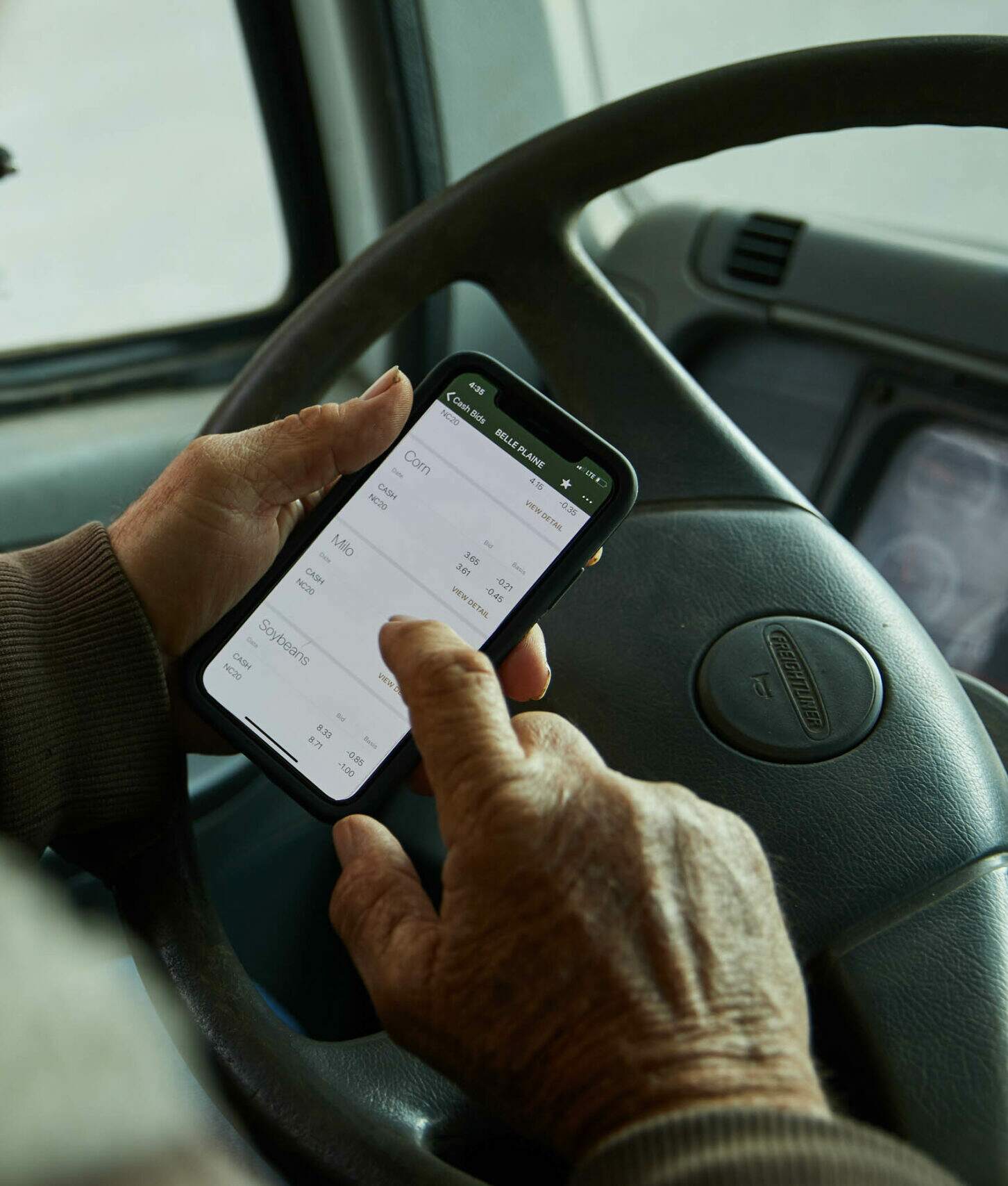 Man looking at a phone in front of a steering wheel while a truck is parked