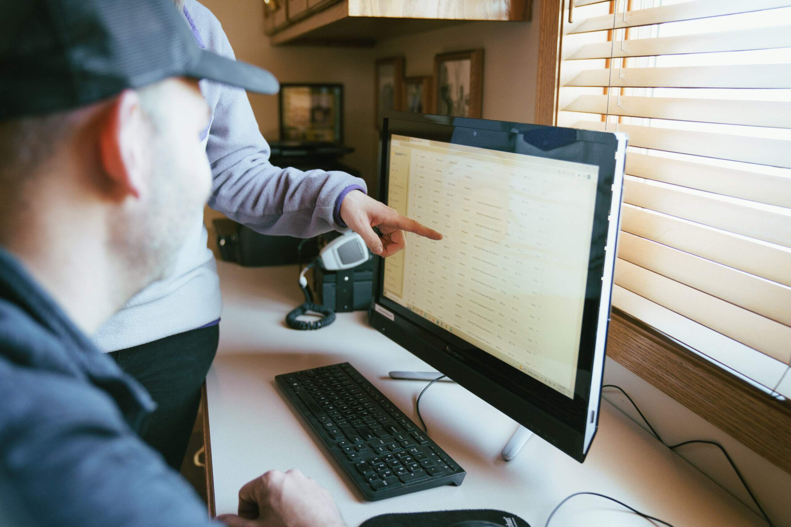 A person pointing to a computer screen while a farmer looks on